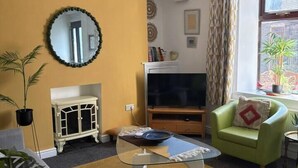 Una sala de estar con televisión, un sofá, una mesa de centro y una ventana con cortinas.
