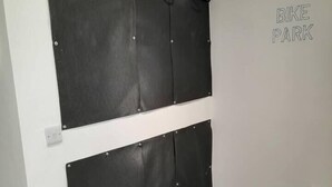 Una habitación con un aparcamiento para bicicletas, un sistema de almacenamiento de bicicletas en la pared y una maleta en el suelo.