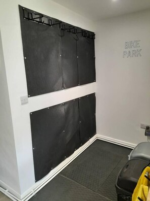 Una habitació amb un aparca bicicletes, un sistema de plegat de bicicleta a la pared i una maleta a terra.