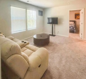 A living room with a beige sofa, a flat-screen TV, and a carpeted floor. - Kinetic Home (Pooler)