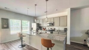 Una cocina moderna con una isla central, taburetes de bar y electrodomésticos de acero inoxidable.