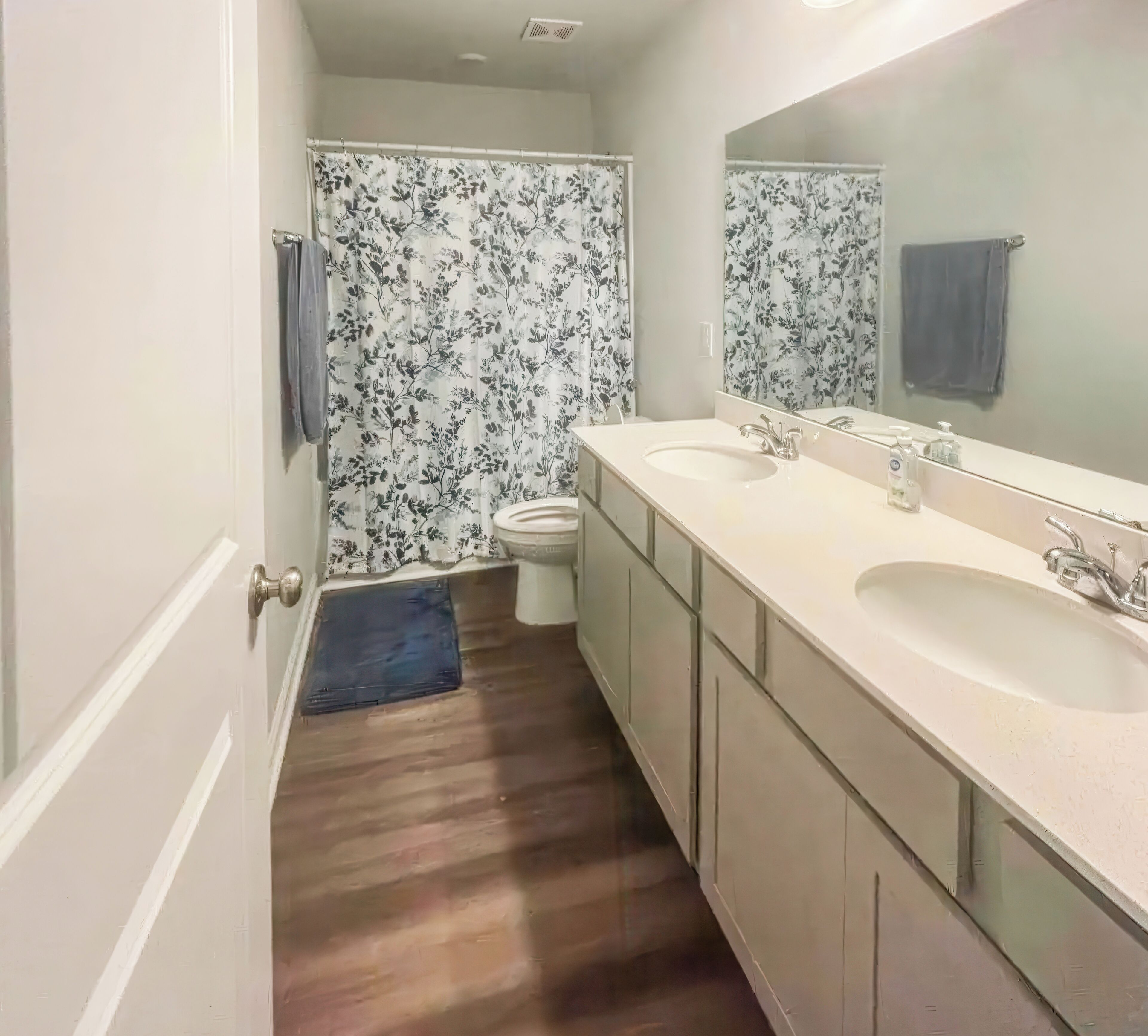 A bathroom with two sinks, a toilet, and a shower curtain with a floral pattern.