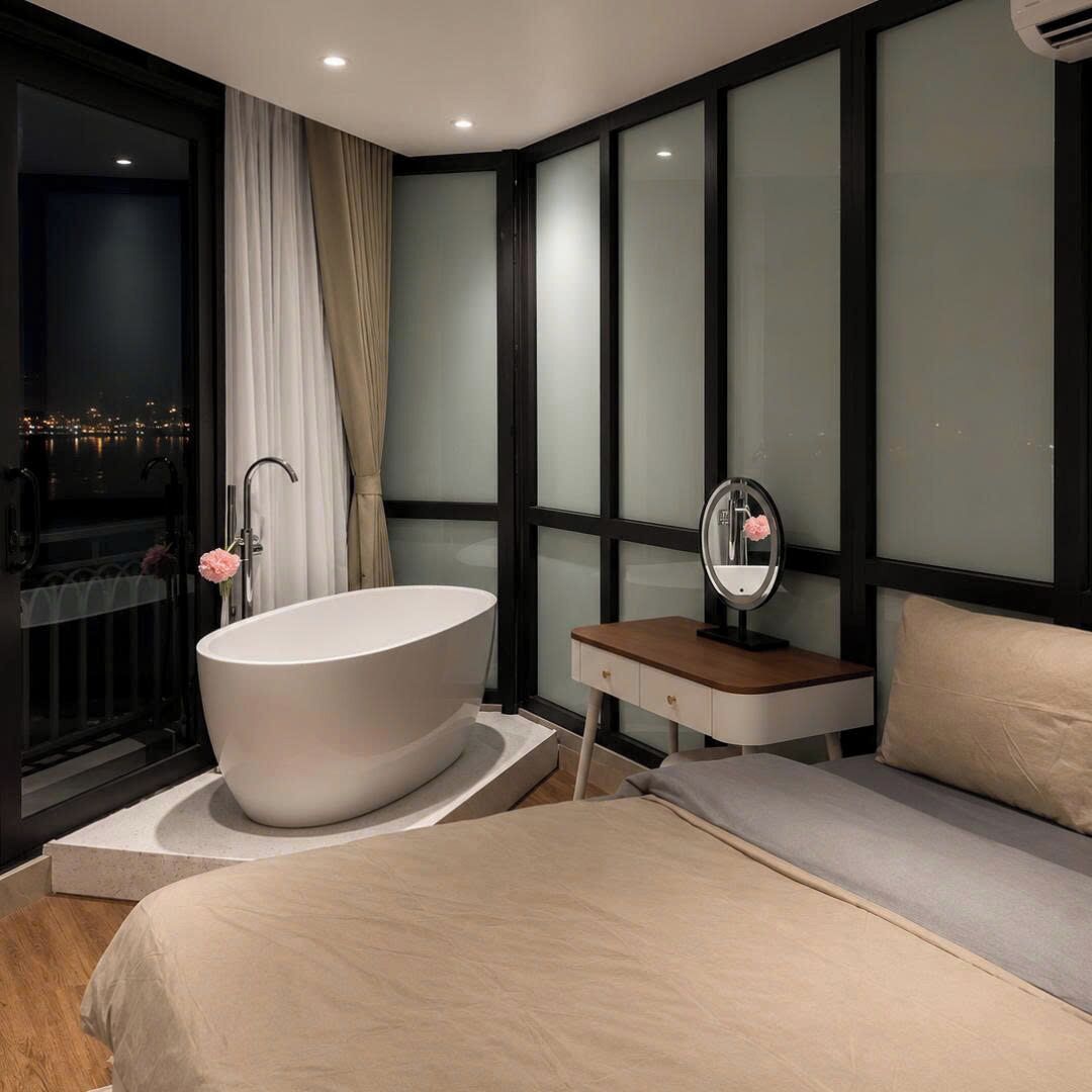 A modern bedroom with a large bathtub, a bedside table with a mirror, and a view of the city at night.