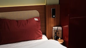 Una camera d'hotel con un letto, un comodino, un telefono fissato al muro e una rivista sul comodino.
