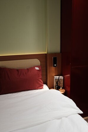 Et hotelværelse med en seng, et natbord, en vægmonteret telefon og et magasin på natbordet.