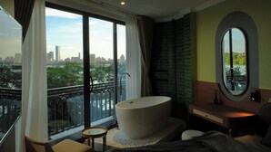 Camera d'albergo con un'ampia finestra che si affaccia su un orizzonte cittadino e una distesa d'acqua.