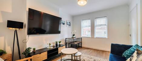 A modern living room with a flat-screen TV, a coffee table, a sofa, and a patterned rug.