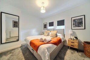Quarto com cama grande, mesa de cabeceira com abajur, radiador e quadros nas paredes.