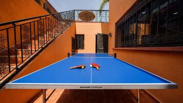 Une table de ping-pong avec deux raquettes et une balle, entourée de murs orange et d’un escalier.