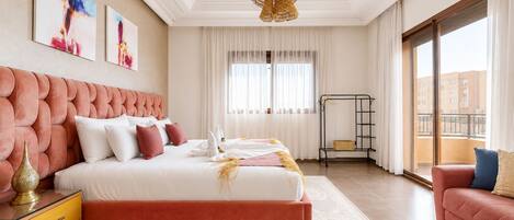 A modern bedroom with a large bed, a bedside table, a decorative lamp, and a view of the outside.