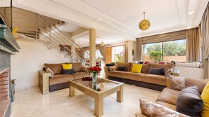 A spacious living room with a large sofa set, a coffee table, and a staircase. - Villa Amroth (Marrakech)
