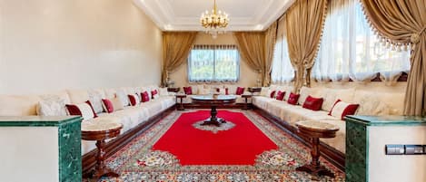 Un salon élégant, avec un tapis rouge, des canapés blancs et un lustre.