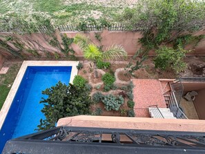 A rooftop pool with a clear blue water surface, surrounded by various plants and trees. - Villa Amroth (Marrakech)