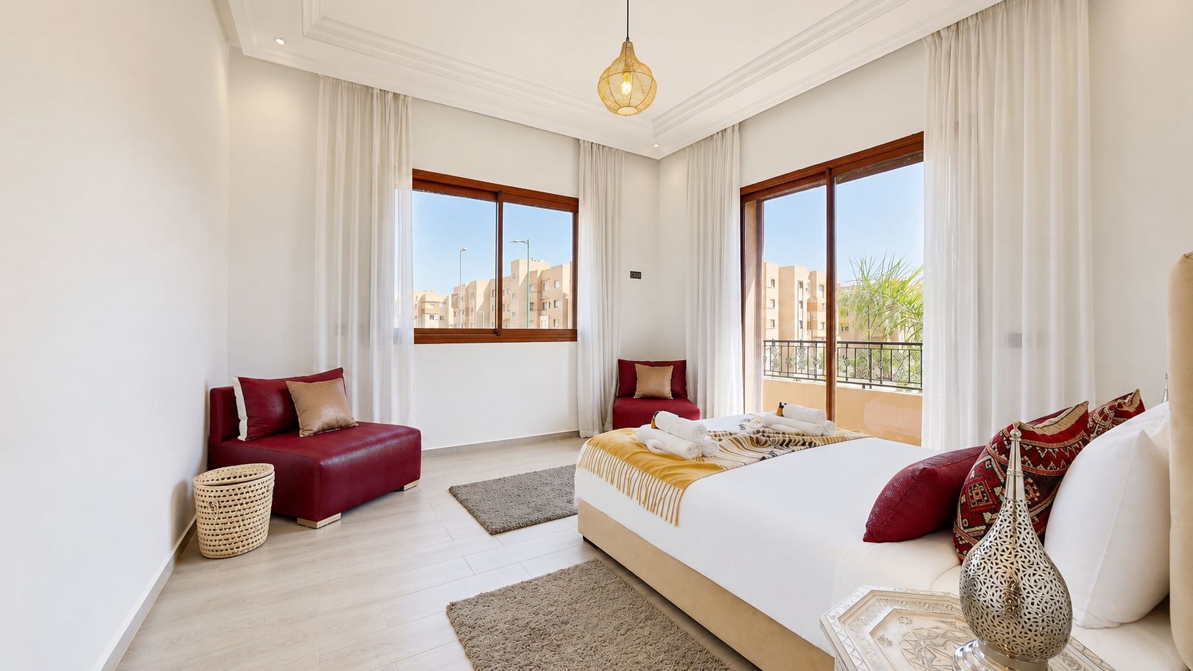 Une chambre d’hôtel avec un grand lit, un canapé rouge et un balcon donnant sur des immeubles.