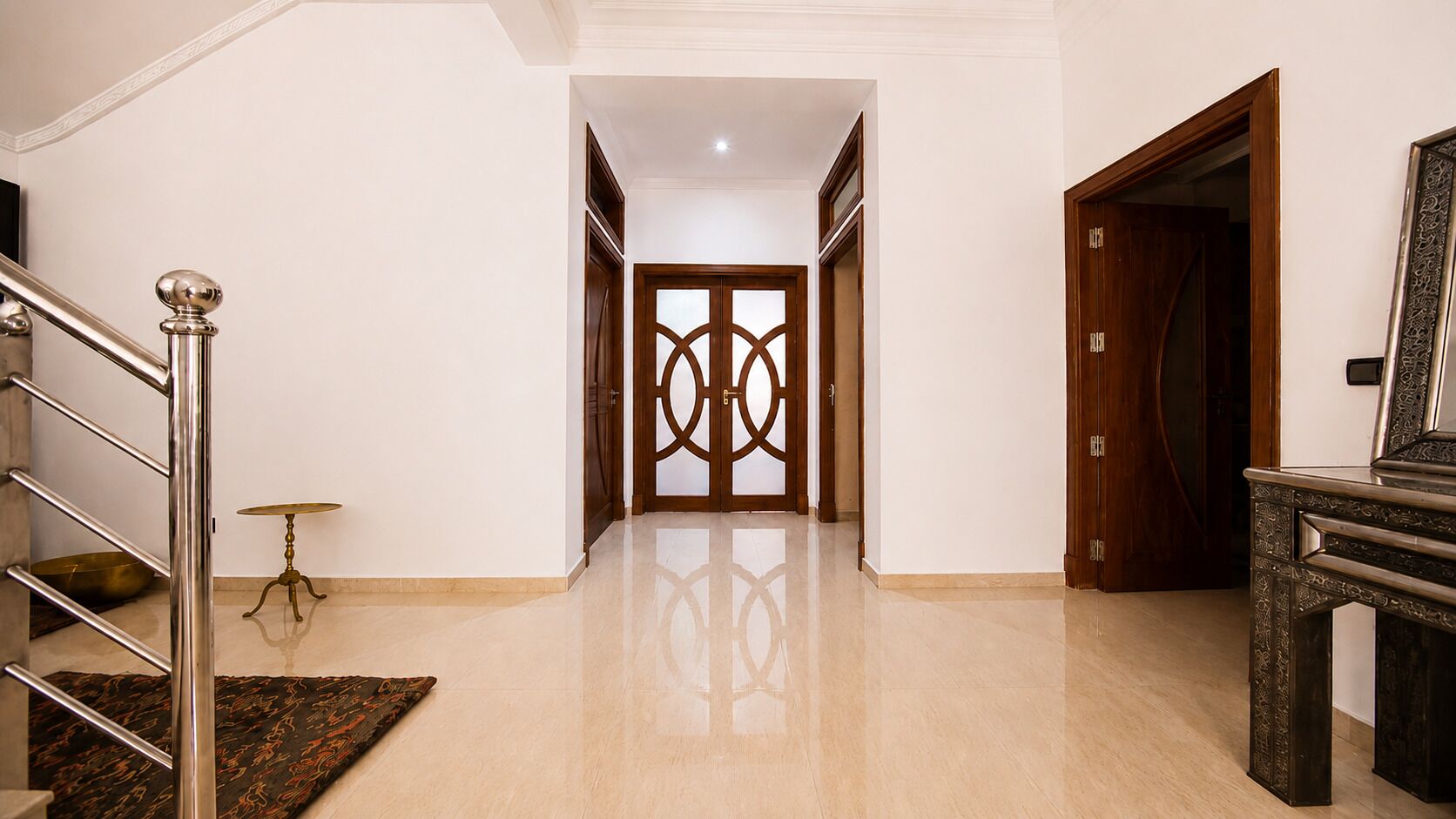 A spacious hallway with a polished floor, a staircase with metal railings, and a wooden door with intricate patterns.