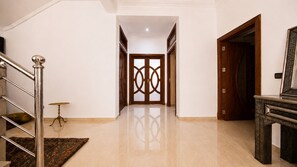 A spacious hallway with a polished floor, a staircase with metal railings, and a wooden door with intricate patterns. - Villa Amroth (Marrakech)