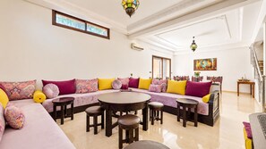 A spacious living room with a large L-shaped sofa, a round coffee table, and multiple chairs. - Villa Amroth (Marrakech)