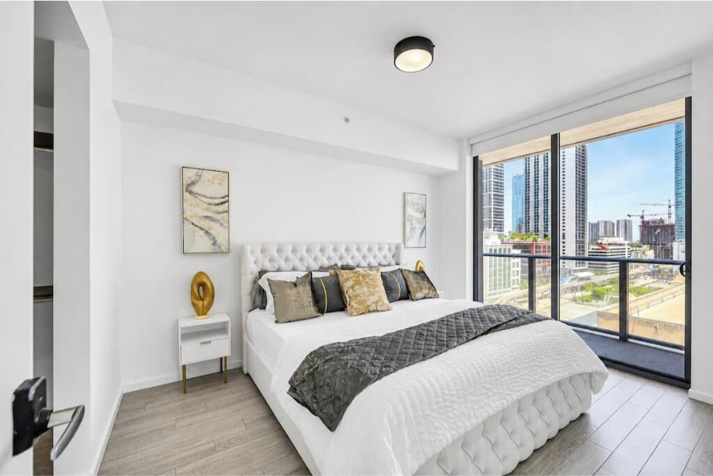 Une chambre moderne avec un grand lit, une table de chevet et une vue sur la ville grâce à de grandes fenêtres du sol au plafond.