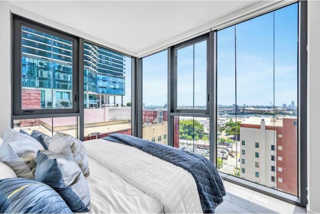 A bedroom with a large window, a bed, and a view of a cityscape.