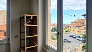 A corner of a room with a wooden shelf against a window, overlooking a street with buildings and parked cars. - City / Village Apartment in Viareggio with 2 bedrooms sleeps 5 (Viareggio)
