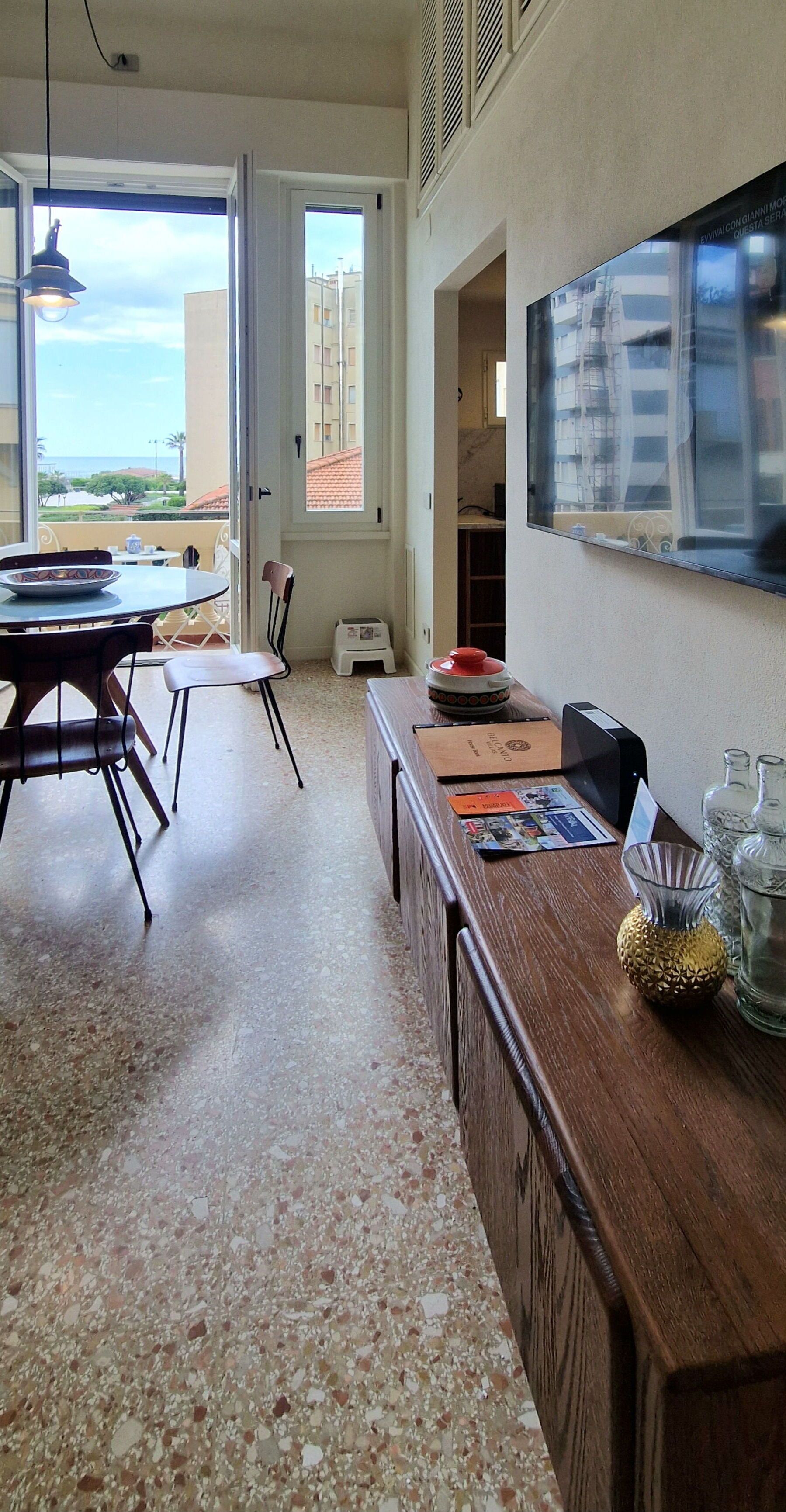 A spacious room with a dining area, a kitchen counter, and a large window offering a view of the sea.