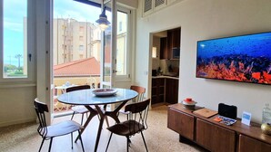 A dining area with a round table, chairs, a television displaying an underwater scene, and a view of buildings outside. - City / Village Apartment in Viareggio with 2 bedrooms sleeps 5 (Viareggio)