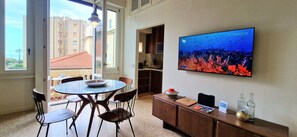 A dining area with a round table, chairs, a television displaying an underwater scene, and a view of buildings outside. - City / Village Apartment in Viareggio with 2 bedrooms sleeps 5 (Viareggio)
