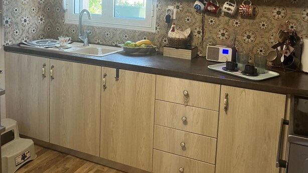 A kitchen with wooden cabinets, a microwave, a window with blinds, and various kitchen items on the counter. - Apartment 'Elea' with Mountain View, Wi-Fi and Air Conditioning (Epanomi)