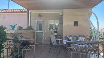 Een terras buiten met een tafel, stoelen, een deur en potplanten.