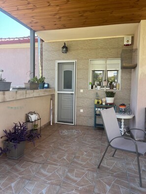 En overdækket terrasse med dør, et vindue med udsigt og et bord med stole.