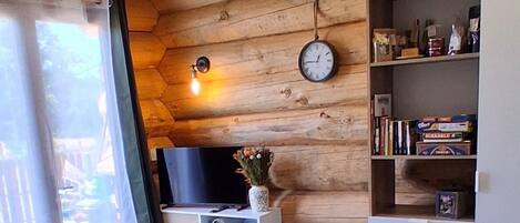 En mysig stuga med träpanel på väggarna, en soffa, ett matbord, en hundbädd, en tv och en bokhylla.