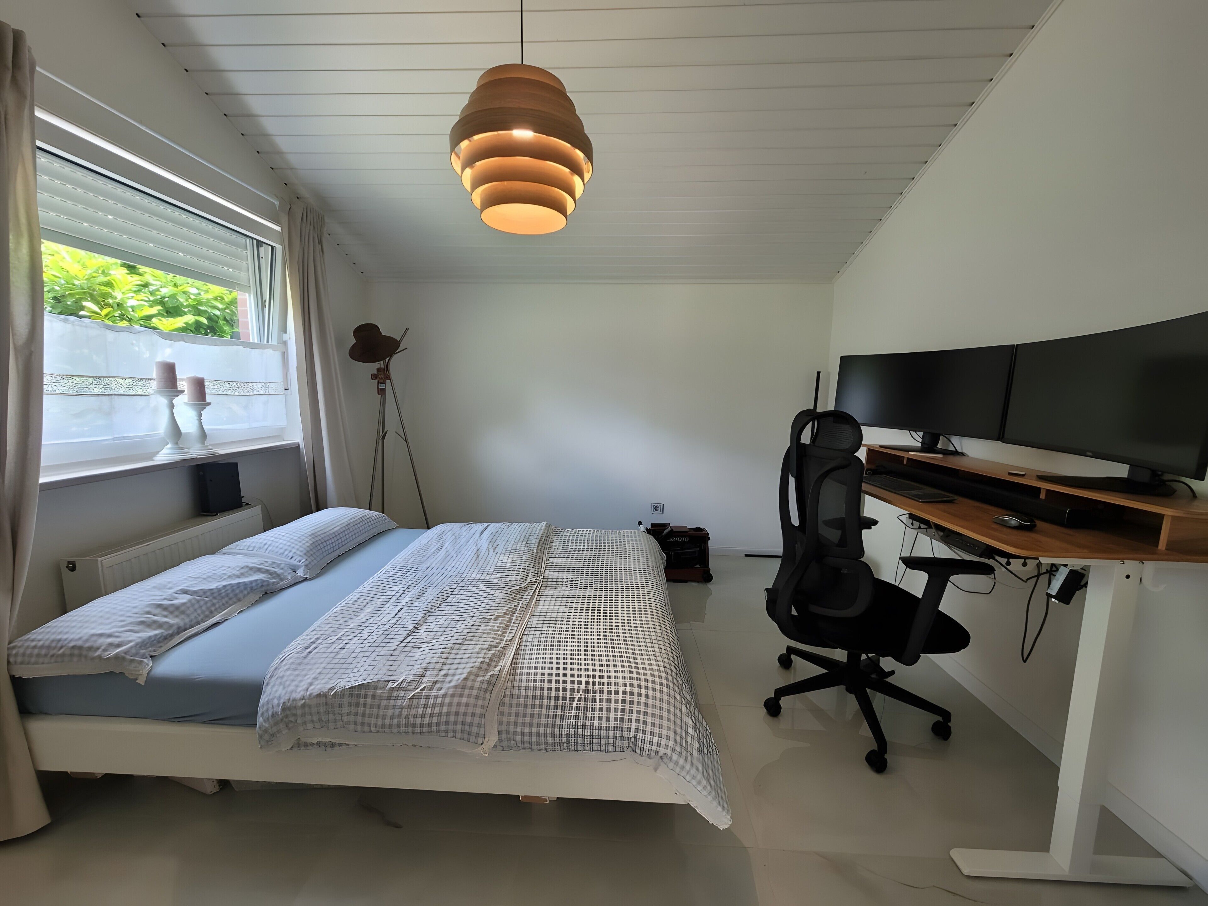 Un dormitorio con una cama, un escritorio con computadora, una silla y un ventanal con cortinas.