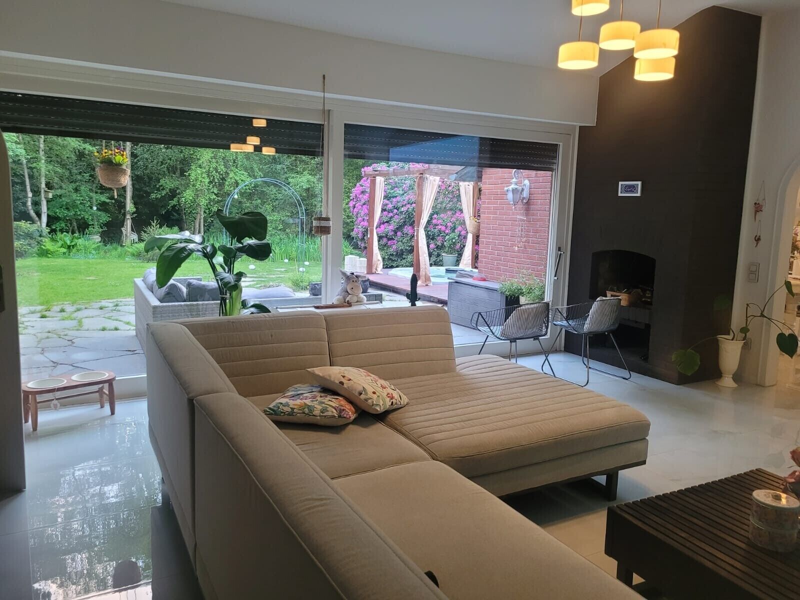 A modern living room with a sectional sofa, a fireplace, and a view of a garden through large windows.
