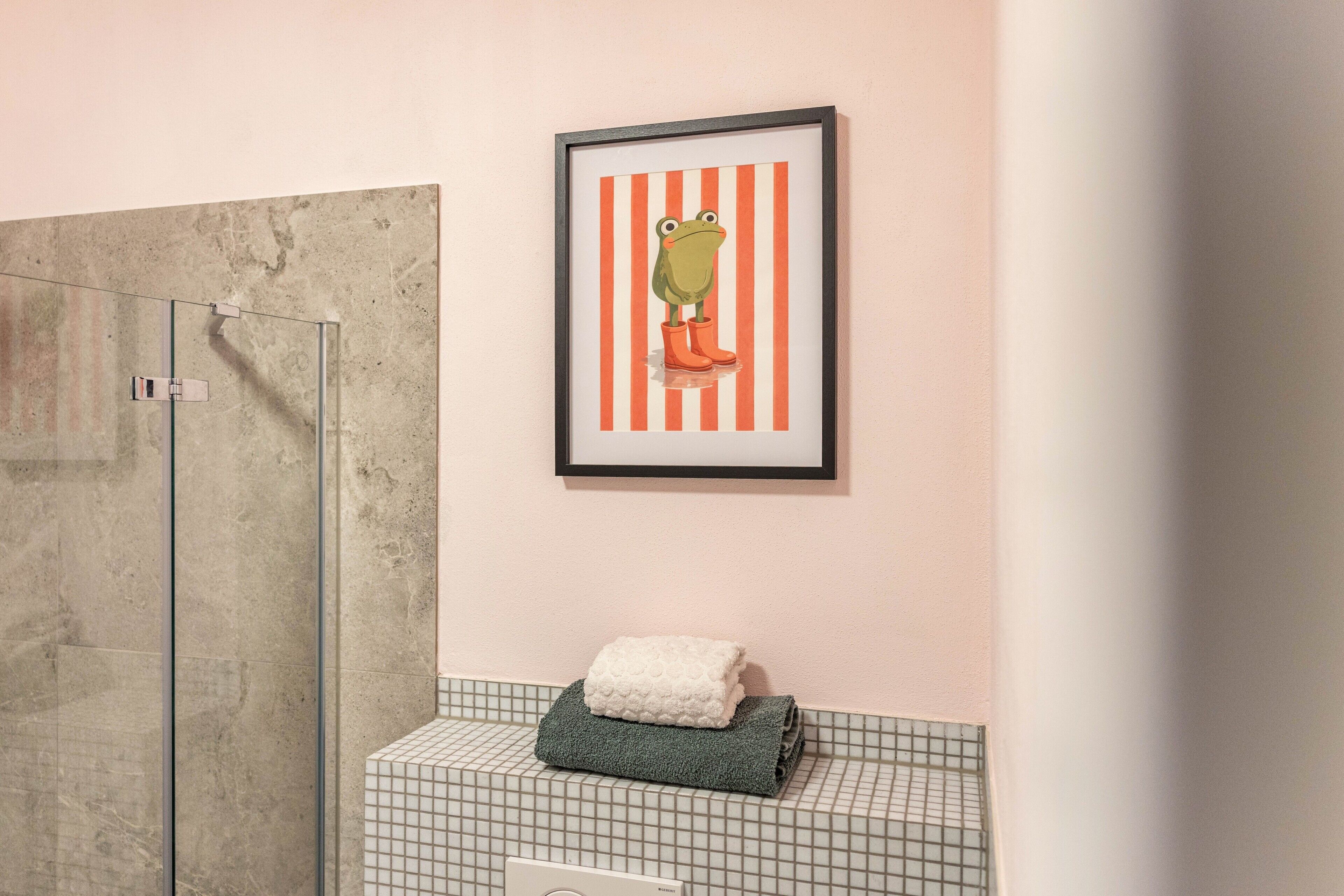 Een badkamer met een glazen douchecabine, een inlijsting foto aan de muur en een handdoekrek met opgevouwen handdoeken.