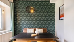 A dining area with a dark table, two wooden chairs, a patterned wall, a hanging light fixture, and a framed picture on the wall. - Suite Maximilian at Alten Berghotel: Mountain Views, Private Terrace & Wi-Fi (Eslohe)