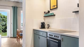 Et kompakt køkken med indbygget ovn, kaffemaskine og spiseplads med bord og stole.