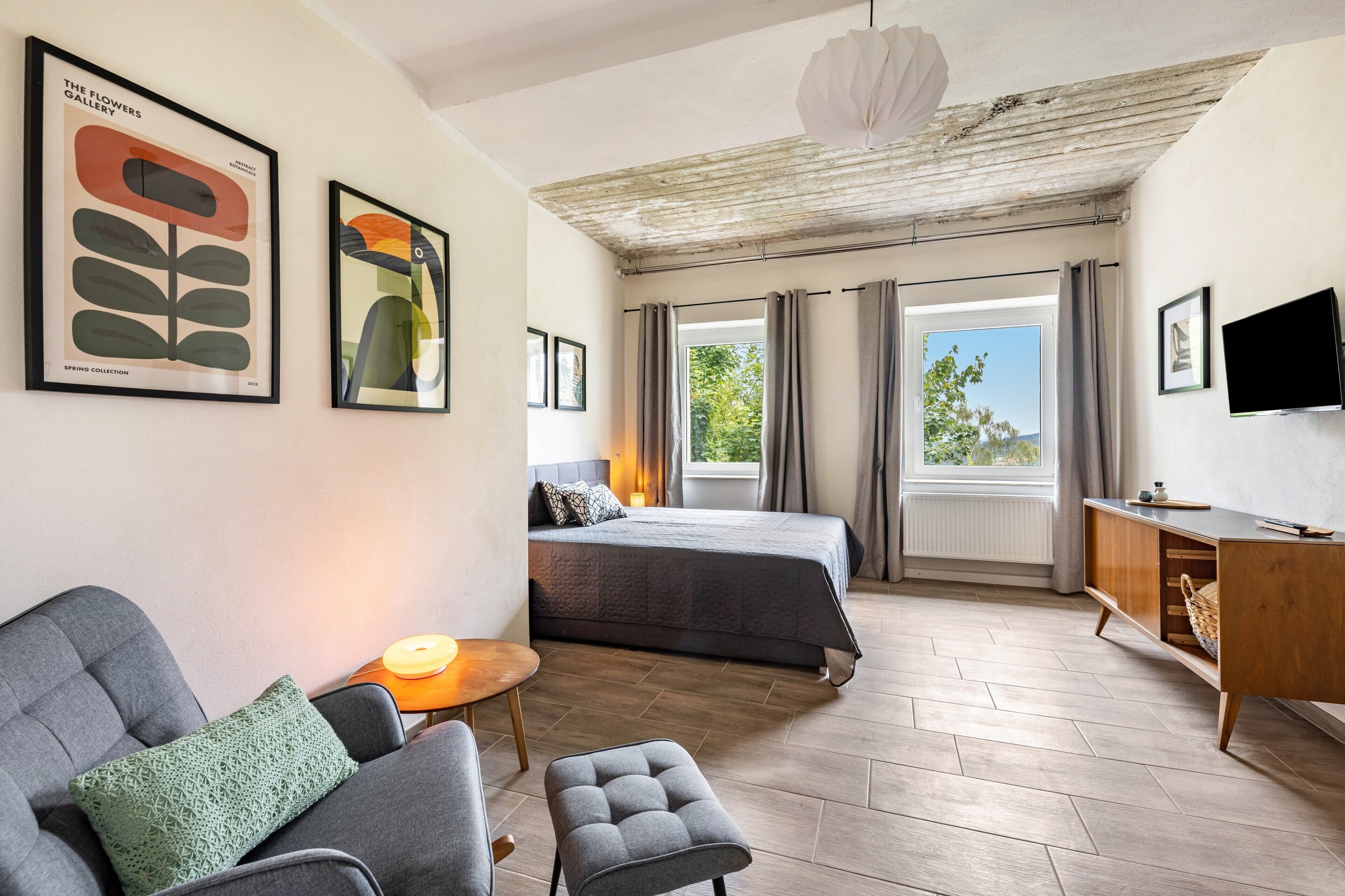 Ett hotellrum med en säng, en soffa, ett litet bord, en tv och konstverk på väggarna.