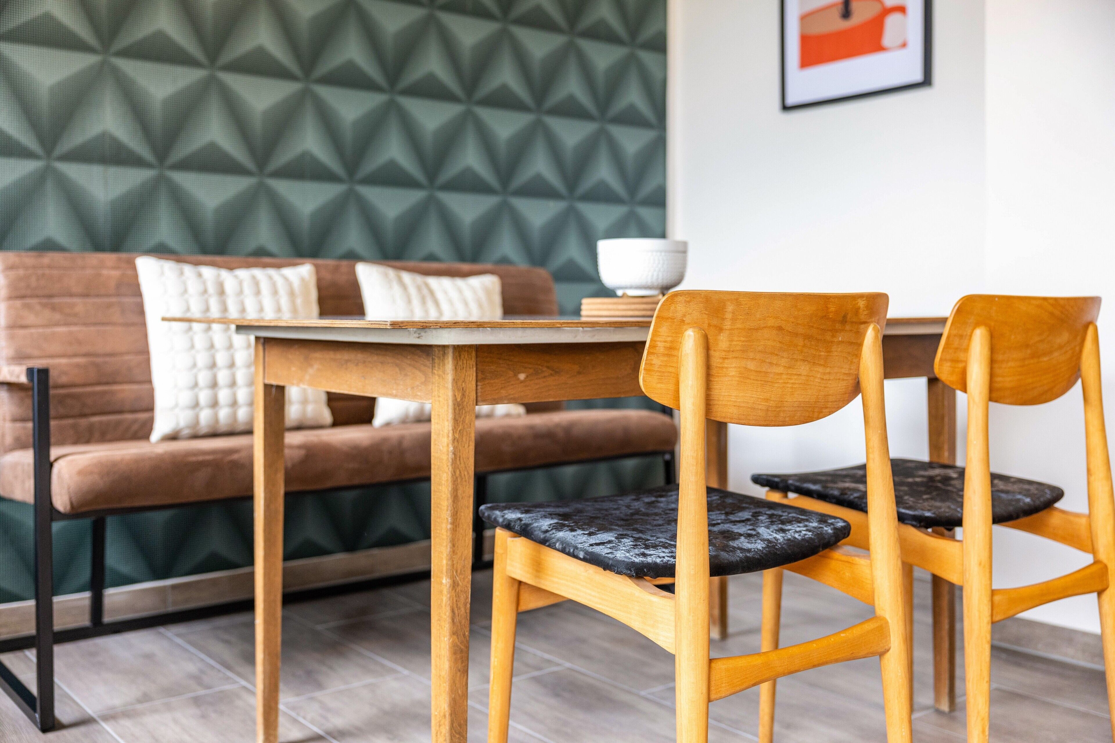 A dining area with a wooden table and chairs, a sofa with cushions, and a geometric patterned wall.