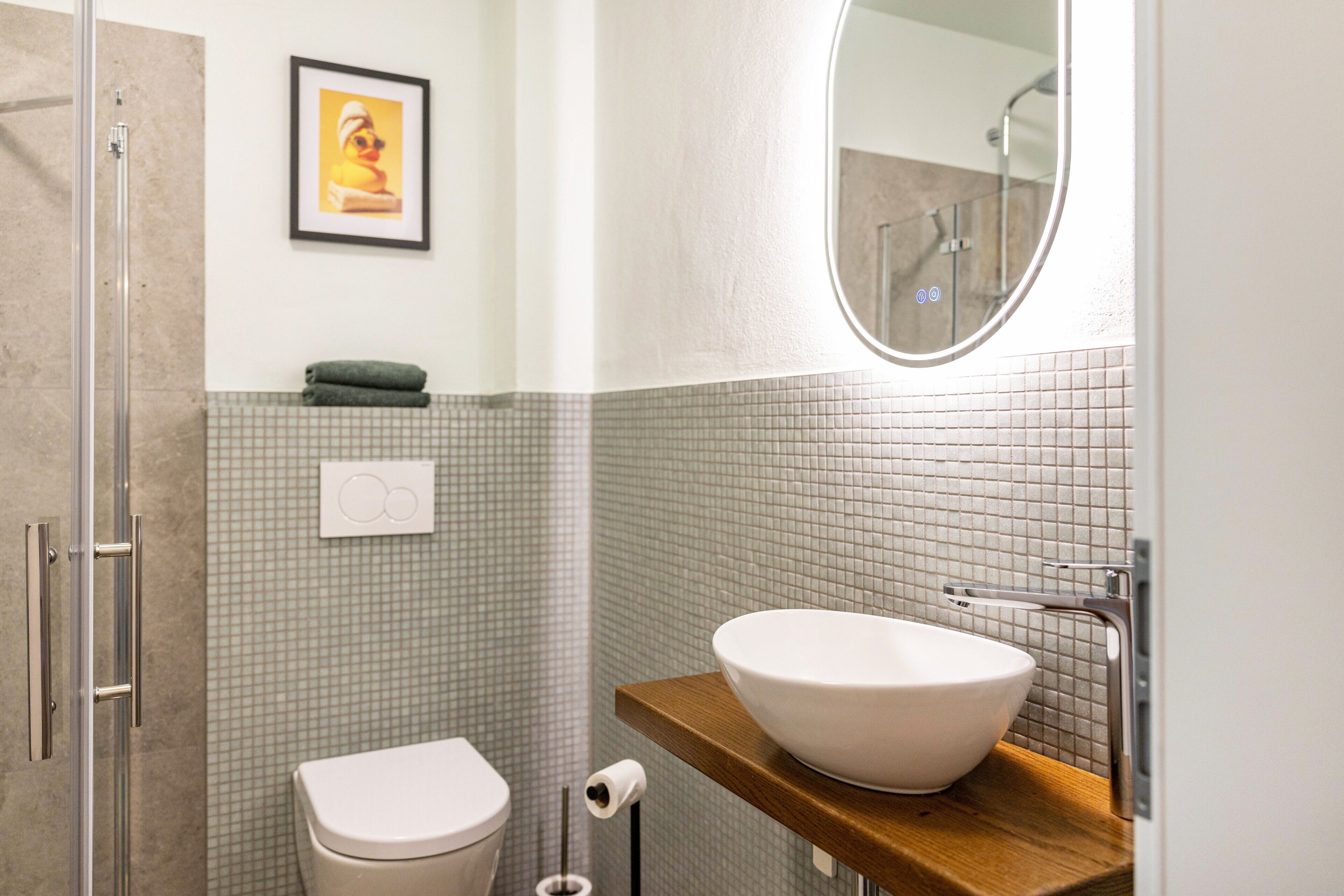 Ein Badezimmer mit Toilette, einem Waschbecken mit Vessel-Becken, einer Duschzone und einem gerahmten Bild an der Wand.