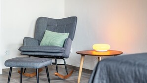A modern room with a grey upholstered chair, a matching ottoman, and a small wooden side table with a yellow lamp. - Suite Maximilian at Alten Berghotel: Mountain Views, Private Terrace & Wi-Fi (Eslohe)