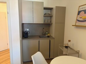 A compact kitchen with a coffee maker, sink, and a small table with a chair. - Charming apartment surrounded by greenery with great access to public transportation (Paderborn)