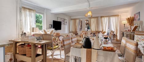 A cozy living room with wicker furniture, a dining table set with food, and a television in the corner.