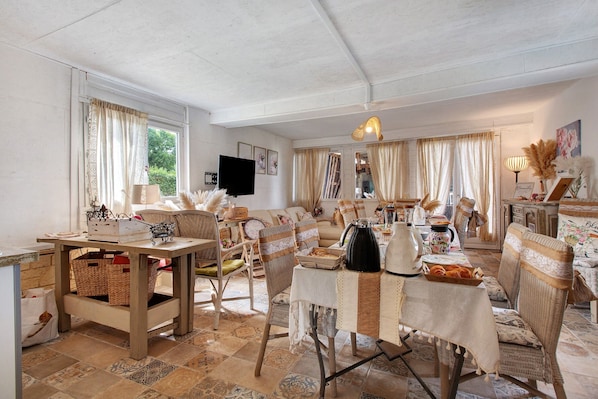 A cozy living room with wicker furniture, a dining table set with food, and a television in the corner.