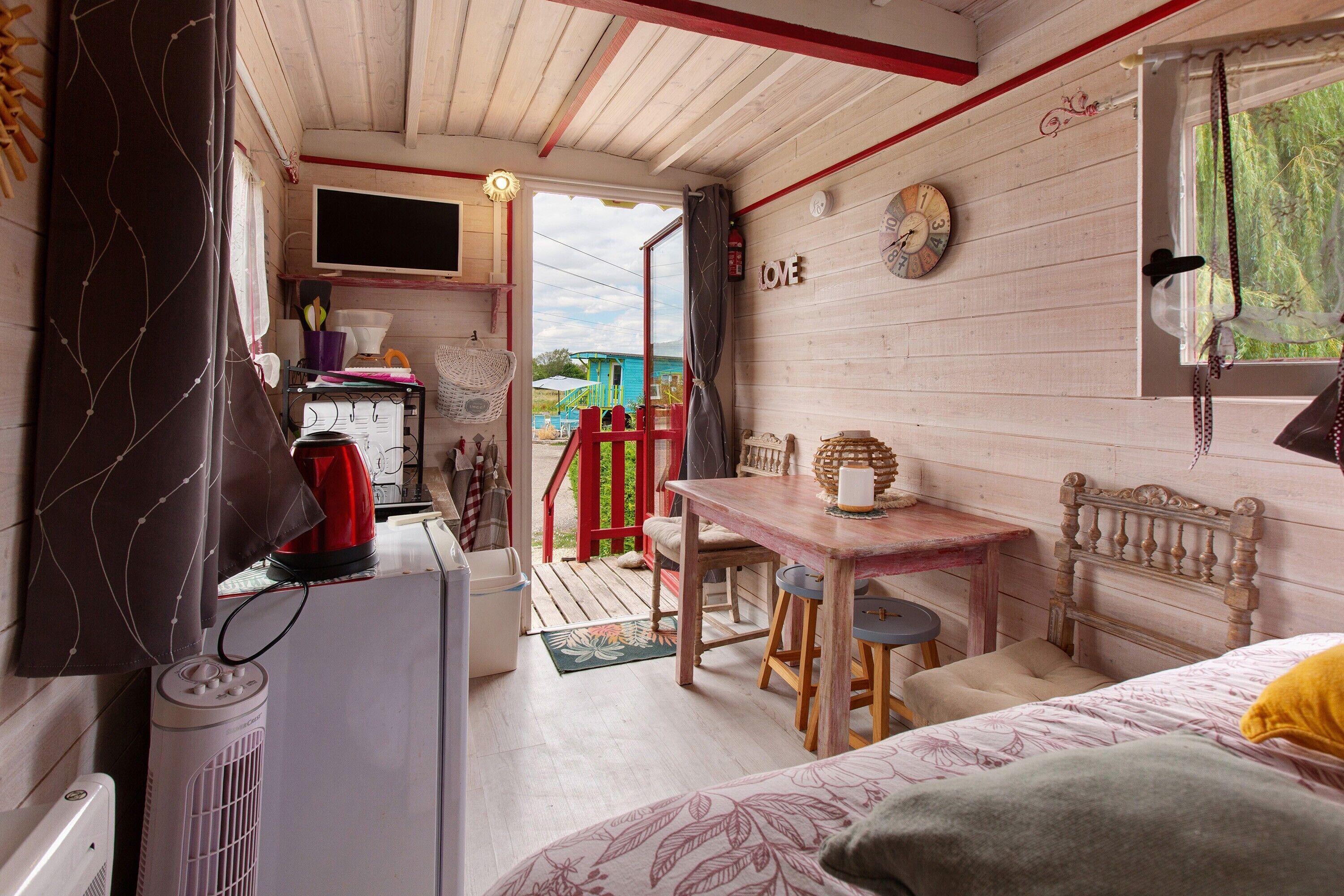A cozy room with a bed, a table, and a chair. There is a window with a view of the outside.