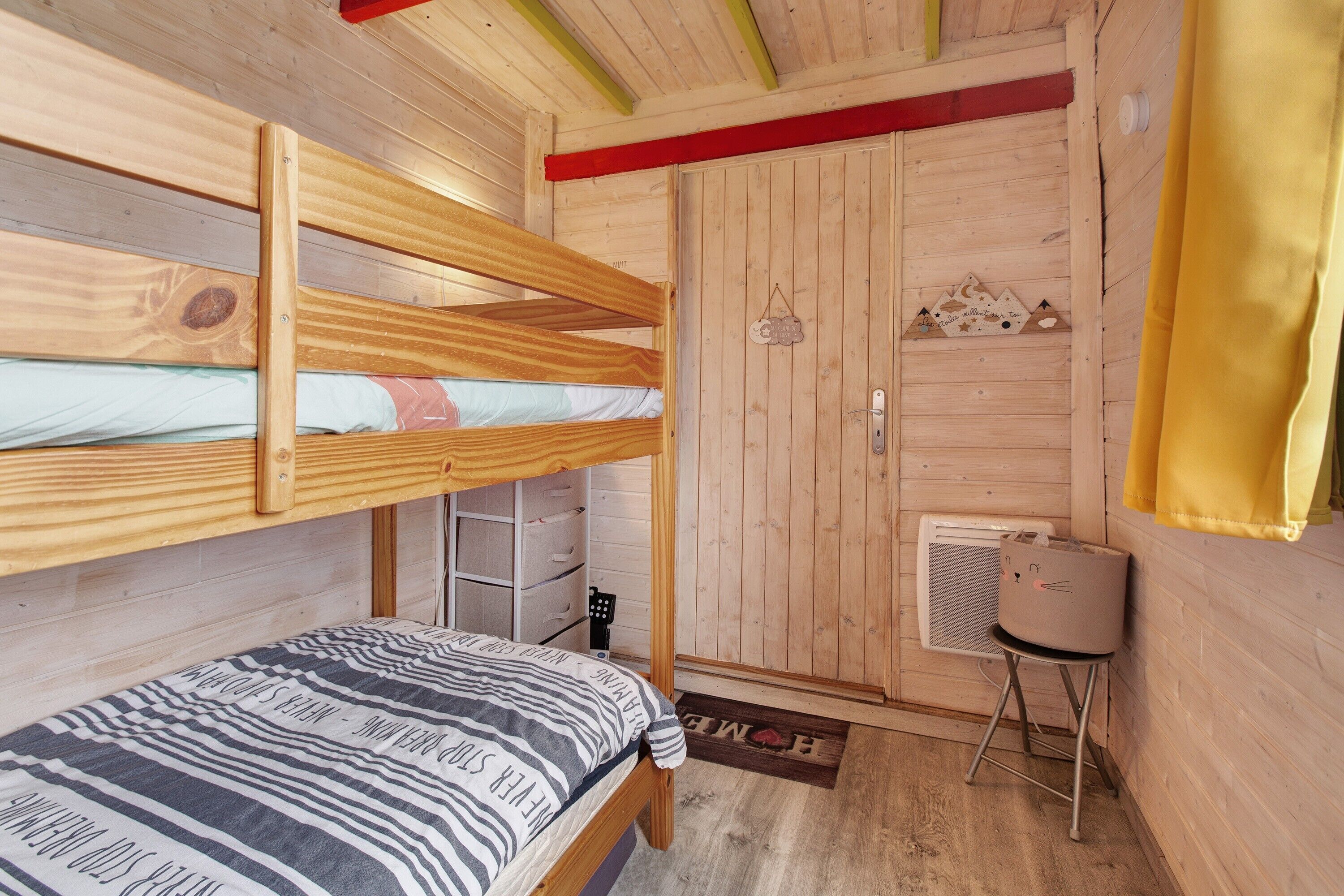 Une chambre avec un lit superposé, une porte en bois et une petite table sur laquelle se trouve un panier.