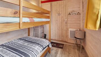 Une chambre avec un lit superposé, une porte en bois et une petite table sur laquelle se trouve un panier.