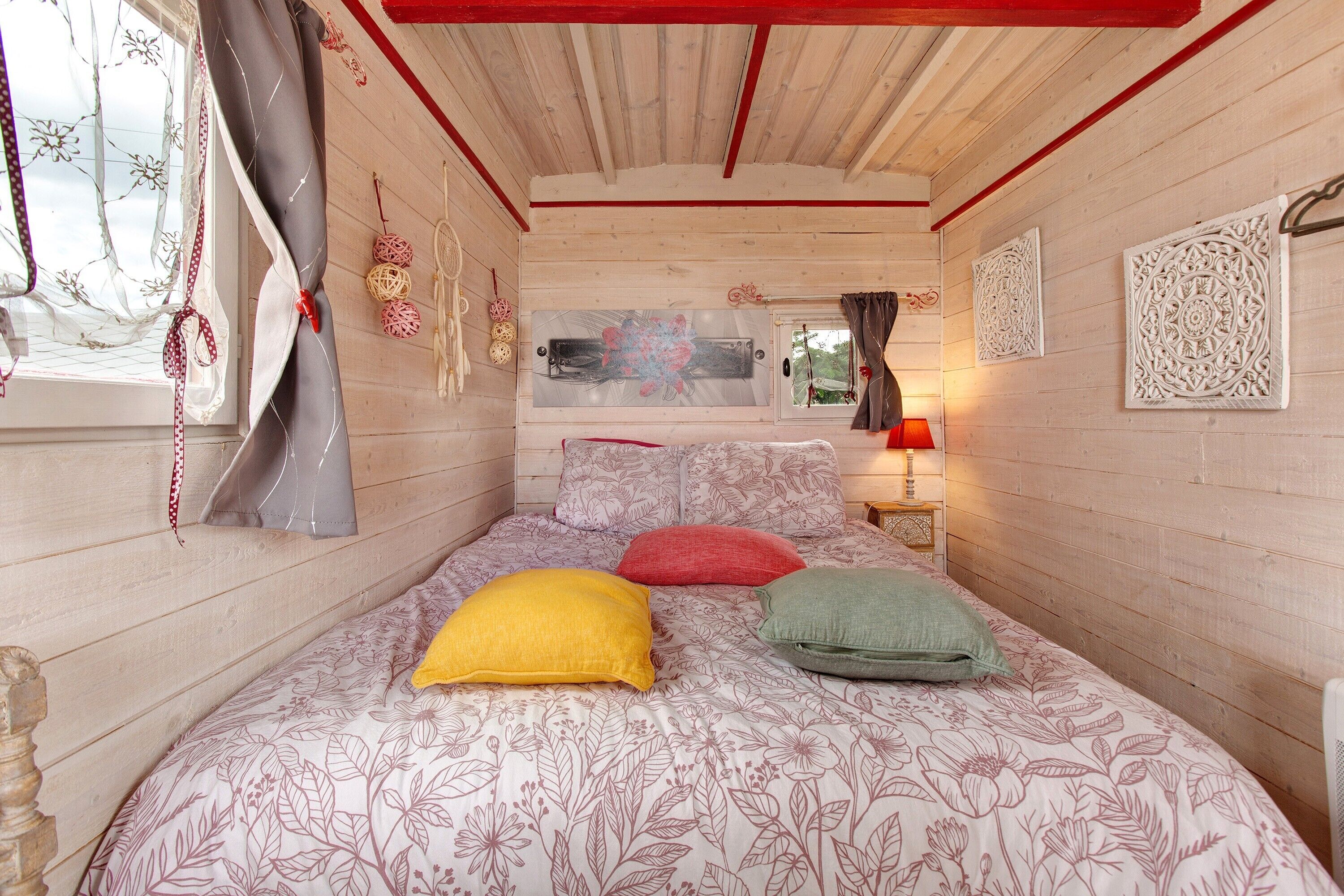 Une chambre avec un lit, une literie à motifs floraux, une fenêtre avec des rideaux et des décorations murales.