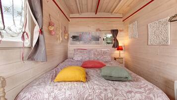 Une chambre avec un lit, une literie à motifs floraux, une fenêtre avec des rideaux et des décorations murales.