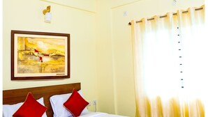 Et hotelværelse med seng, ventilator, et billede på væggen og et vindue med gardiner.