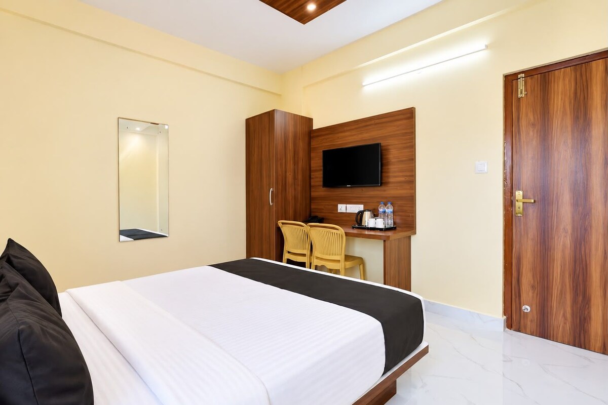 Quarto de hotel com cama, escrivaninha com cadeiras, televisão e guarda-roupa.